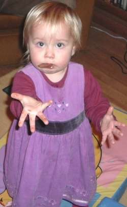 Lily holds out her hand with the chocolate protruding from her mouth.